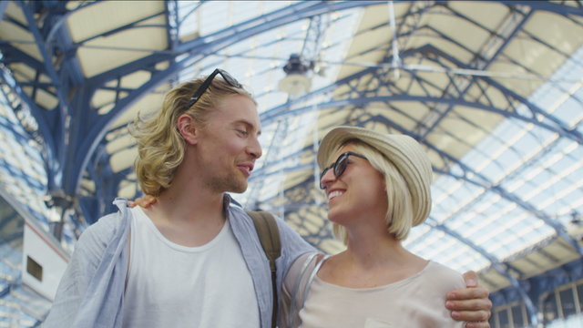 Young couple in love walk arm in arm through a train station talking happily