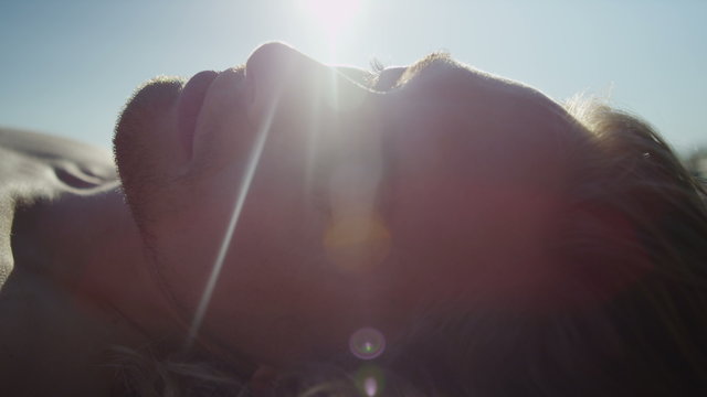 Close up of attractive male's face turning away from the sun as he lays down