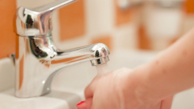 Woman washing her hands at the sink in colorful white and orange tiled bathroom