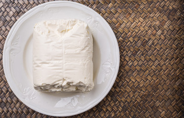 A block of cream cheese on a white plate over wicker background