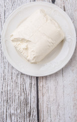 A block of cream cheese on a white plate over weathered wooden background
