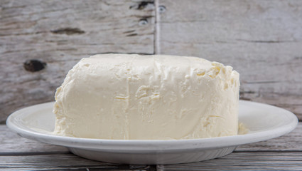 A block of cream cheese on a white plate over weathered wooden background