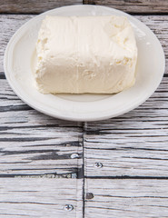 A block of cream cheese on a white plate over weathered wooden background