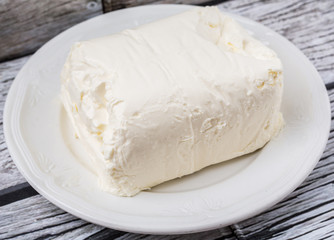 A block of cream cheese on a white plate over weathered wooden background