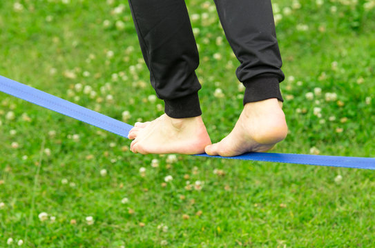 Closeup Man Feet Walking On Slackline And Grassy Background Shot From Side Behind