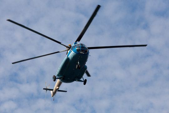 The helicopter flies against the blue sky with clouds