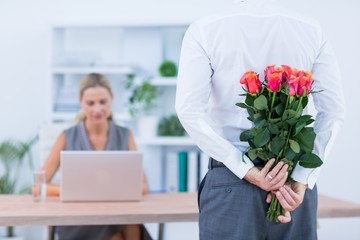 Businessman hiding flowers behind back for colleague 