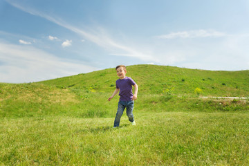 Naklejka na ściany i meble happy little boy running on green field outdoors