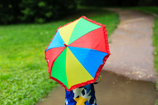 little boy hiding behind colorful umbrella outdoors