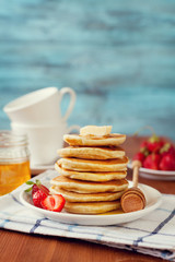 Stack of pancakes with honey syrup, butter and strawberry in a white plate on a wooden rustic table, selective focus, vintage toning