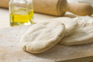 Raw pita bread on on a wooden cutting board.