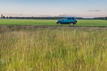Fototapeta premium Rural grassland landscape with green off-road car