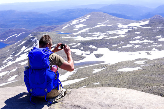 Hiker with big traveling rucksack taking pictures on the phone