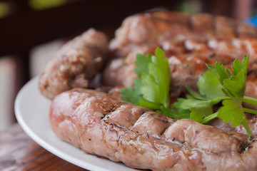 Grilled sausages closeup on a plate with greenery