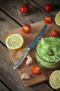 Guacamole on wooden table surrounded by its ingredients..