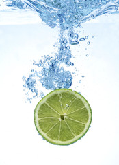 slice of lime droped in the water above white background