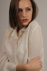 The young gentle beautiful girl with a short hairstyle in a white blouse looks thoughtfully