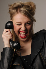 the beautiful cheerful young girl with a fair hair in a leather jacket in red lipstick laughs and speaks by old phone