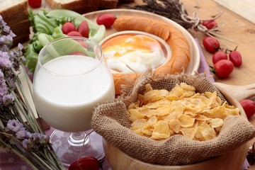 Breakfast with eggs, sausage, bread, salad vegetables and milk.