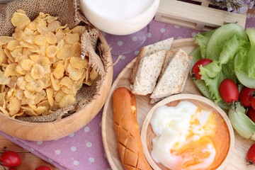 Breakfast with eggs, sausage, bread, salad vegetables and milk.