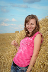 Beautiful girl with ear in hand near the haystack