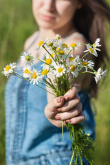 Young brunette girl with long hair holds a bouquet of wild flowers, selective focus