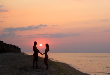 Fototapeta premium couple silhouette holding hands on the beach at sunrise