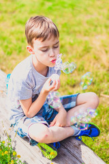 Boy sitting on a bench and blowing soap bubbles