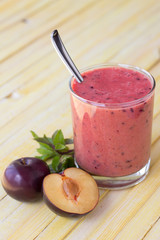 Plum smoothie with fresh plums and mint on yellow toned wooden surface
