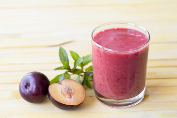 Plum smoothie with fresh plums and mint on yellow toned wooden surface