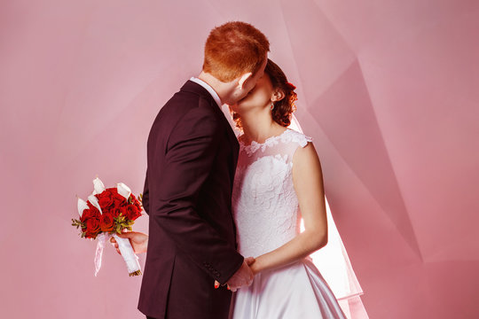 Portrait of beautiful young wedding couple kissing at pink wall