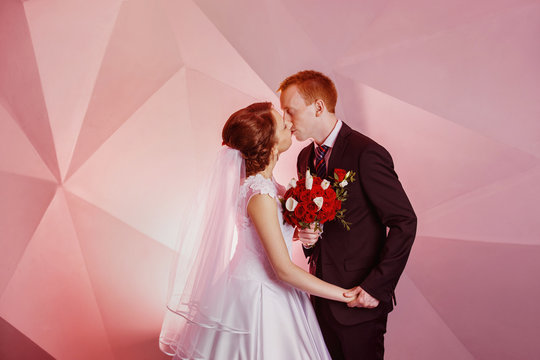 Portrait of beautiful young wedding couple kissing at pink wall