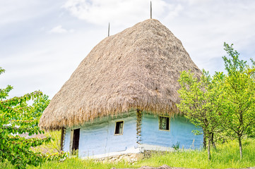 Fototapeta na wymiar Light blue old clay house with a thatched roof, exposed wooden beams and stone foundation.