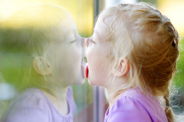 Funny girl licking her reflection on a window - obrazy, fototapety, plakaty