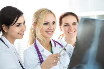 Three smiling female medicine doctor looking at x-ray picture. Healthcare and medicine concept.