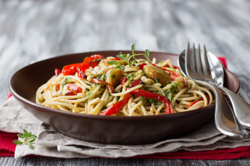 Pasta with baked sweet pepper, garlic, herb oil and pine nuts in a ceramic bowl on the wooden table