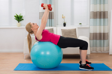 Fototapeta na wymiar Woman With Dumbbell While Exercising On Fitness Ball