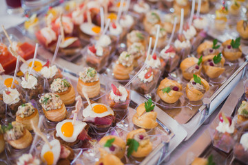 Beautifully decorated catering banquet table with different food snacks and appetizers with sandwich, caviar, fresh fruits on corporate birthday party event or wedding celebration 