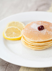 Stack of homemade pancakes with lemon on wood table