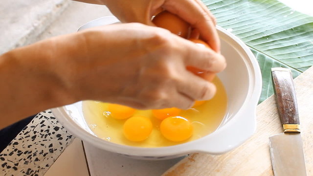 Breaking the eggs in white bowl for Thai dessert making. Food ingredient preparation in local kitchen.