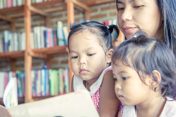 Obraz premium Mother and little daughter reading book together in library