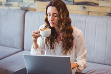 Pretty brunette having coffee using laptop