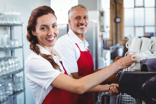 Smiling barista using the coffee machine with colleague behind