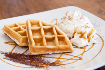 Two waffles on dish, decorated with caramel sauce and whipping cream on wood table