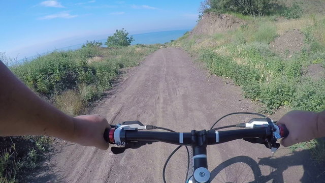 First-person POV Man riding mountain bike on trail along wild sea shore