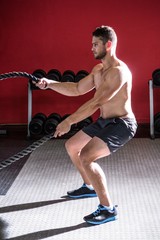 Naklejka na ściany i meble Muscular man exercising with rope