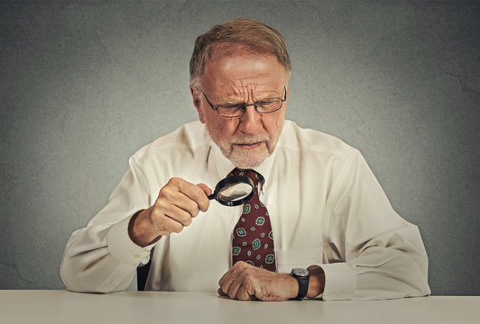 Senior grumpy businessman looking through magnifying glass