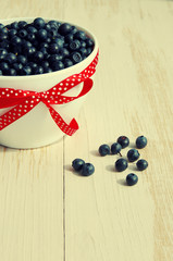 Fresh bilberry in a white ceramic bowl with a red bow on a wooden surface