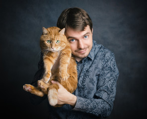 Beautiful young man in shirt hugging his red cat on grey background.