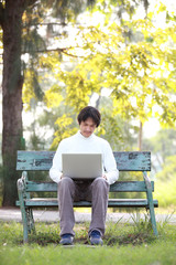 Fototapeta premium A young handsome man using laptop sitting on a bench in a park.